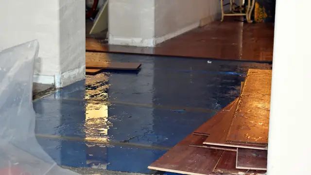 Wet subfloor with hardwood planks lifted and plastic sheeting along the edge
