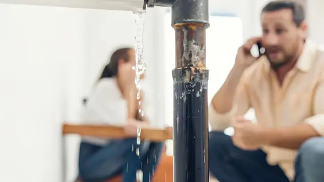 Man on the phone beside a leaking pipe while a woman looks on